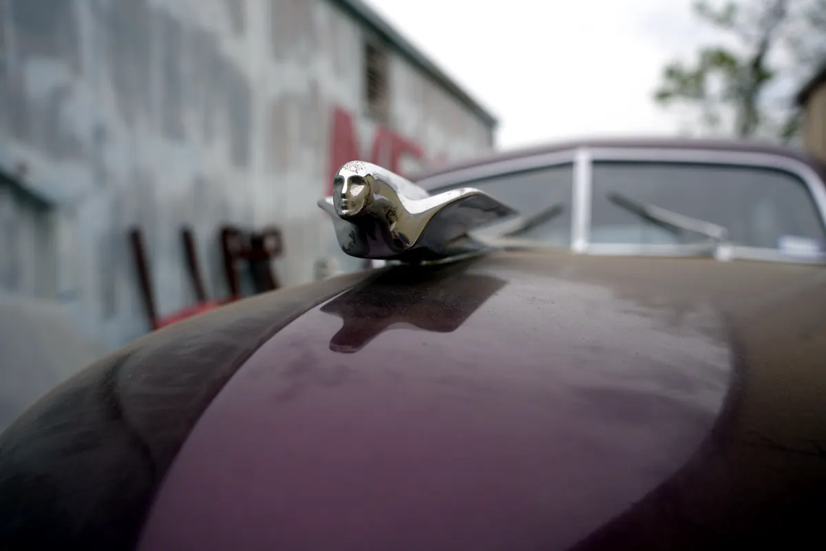 Chrome hood ornament on a burgundy classic outside the shop